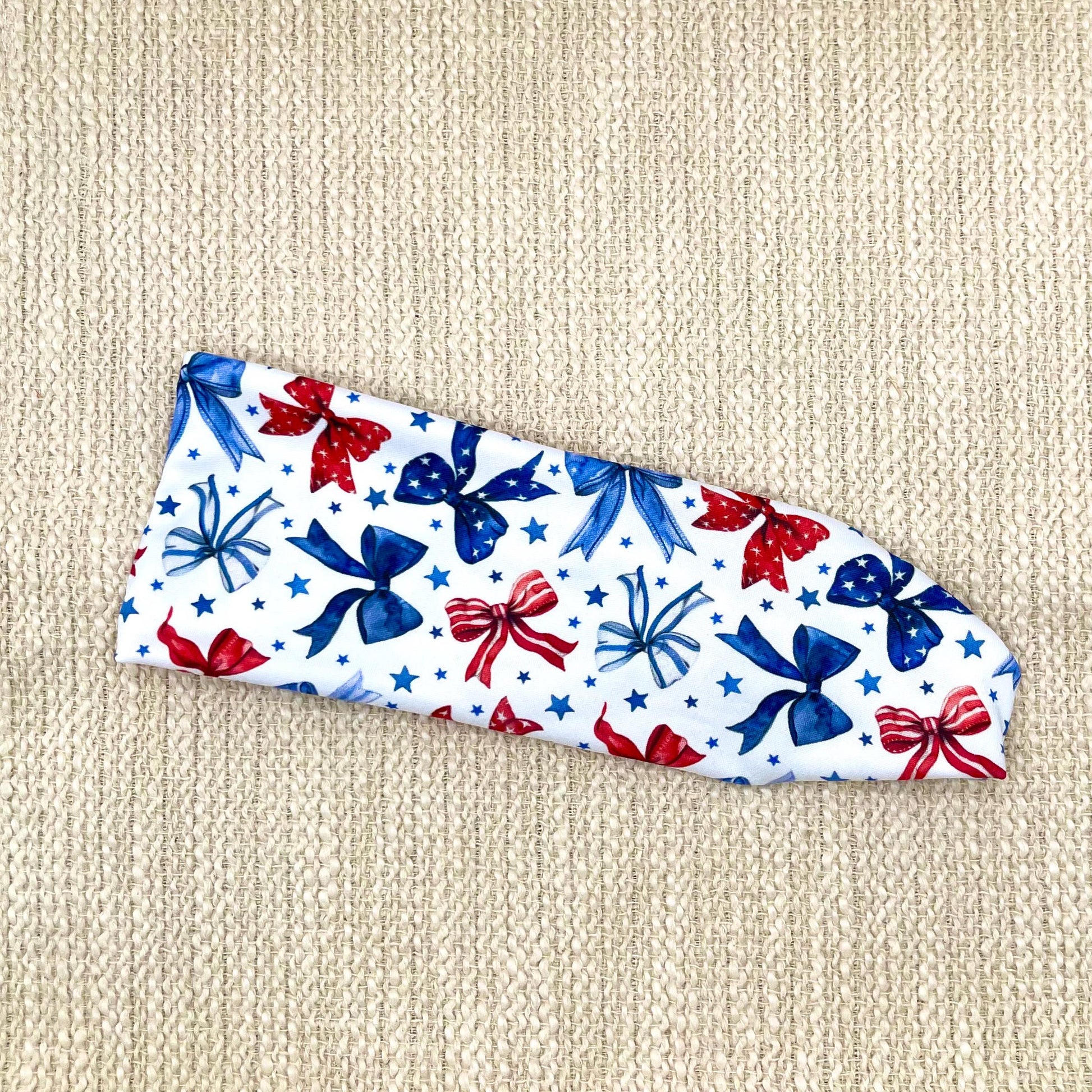 Flat, stretchy, white headband with red and blue bow print and blue stars.