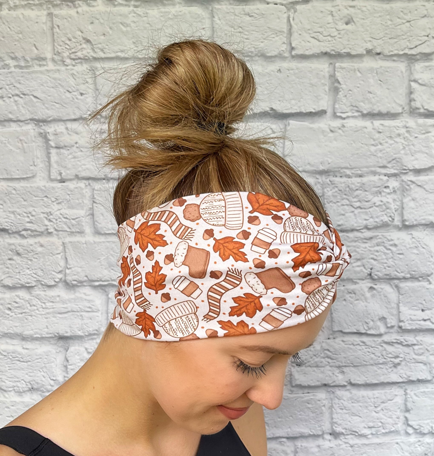Woman with hair in bun wearing wide, twisted headband in light brown with leaves, coffee, hats, and gloves print.