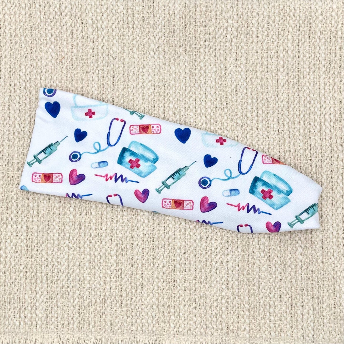 Flat, stretchy, white headband with pink, blue, and purple medical theme print.