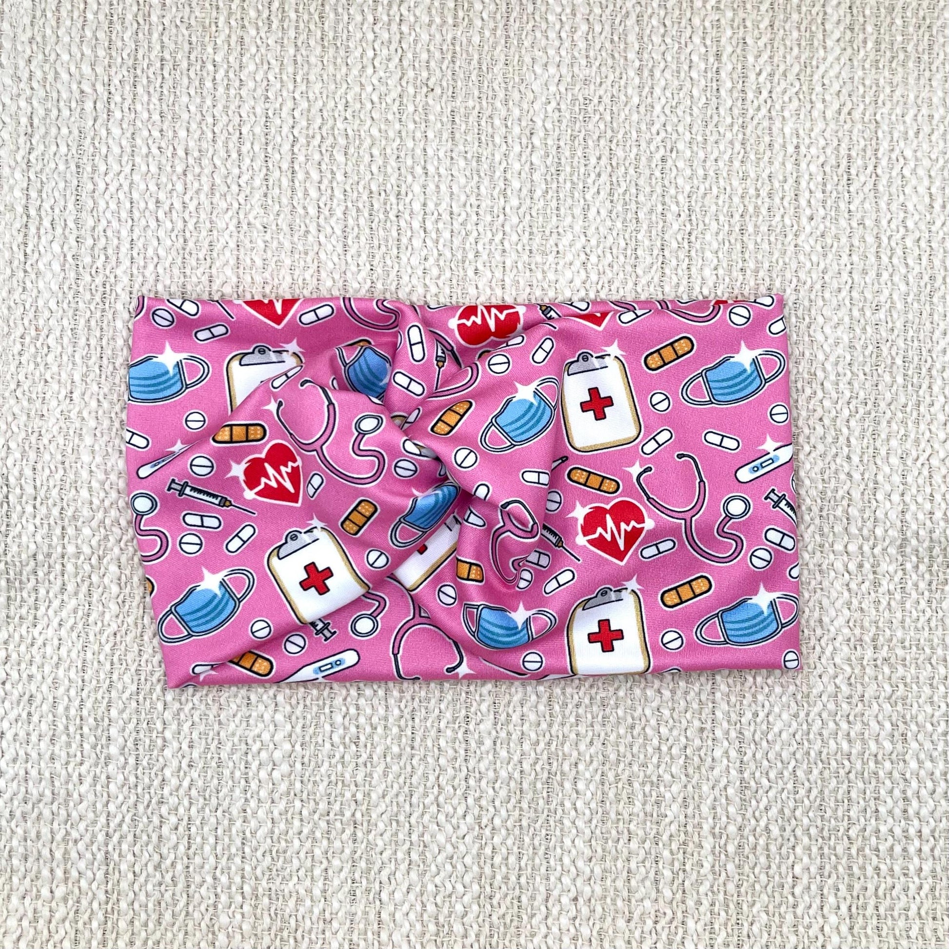 Wide, twisted, stretchy headband in pink with medical theme print.