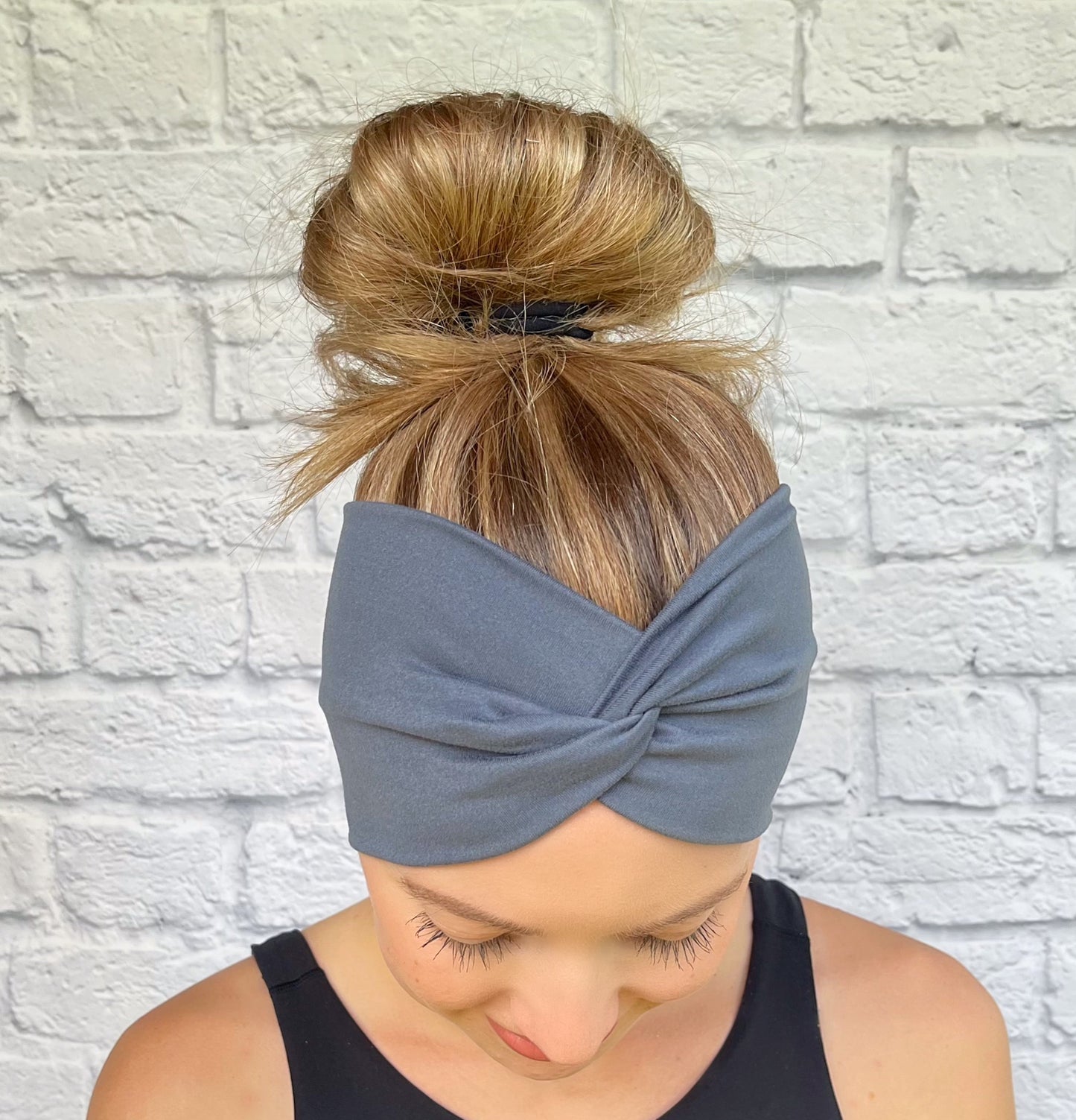 Woman with hair in bun wearing wide, twisted headband in charcoal gray.