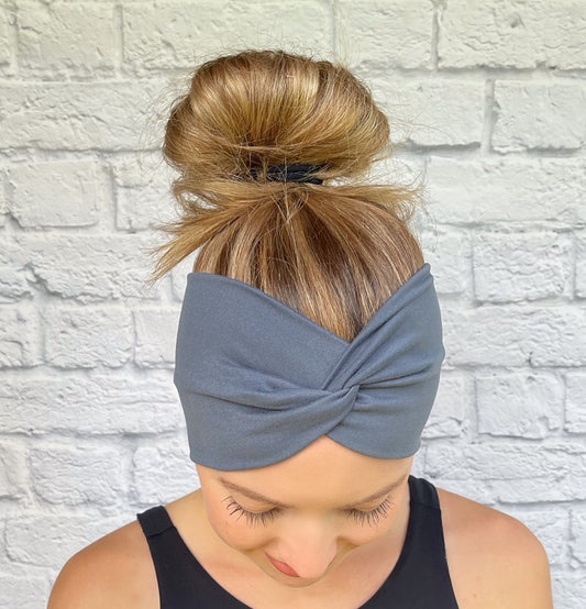 Woman with hair in bun wearing wide, twisted headband in charcoal gray.