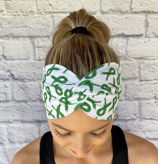Woman with hair in ponytail wearing wide, twisted, white headband with green ribbon print.