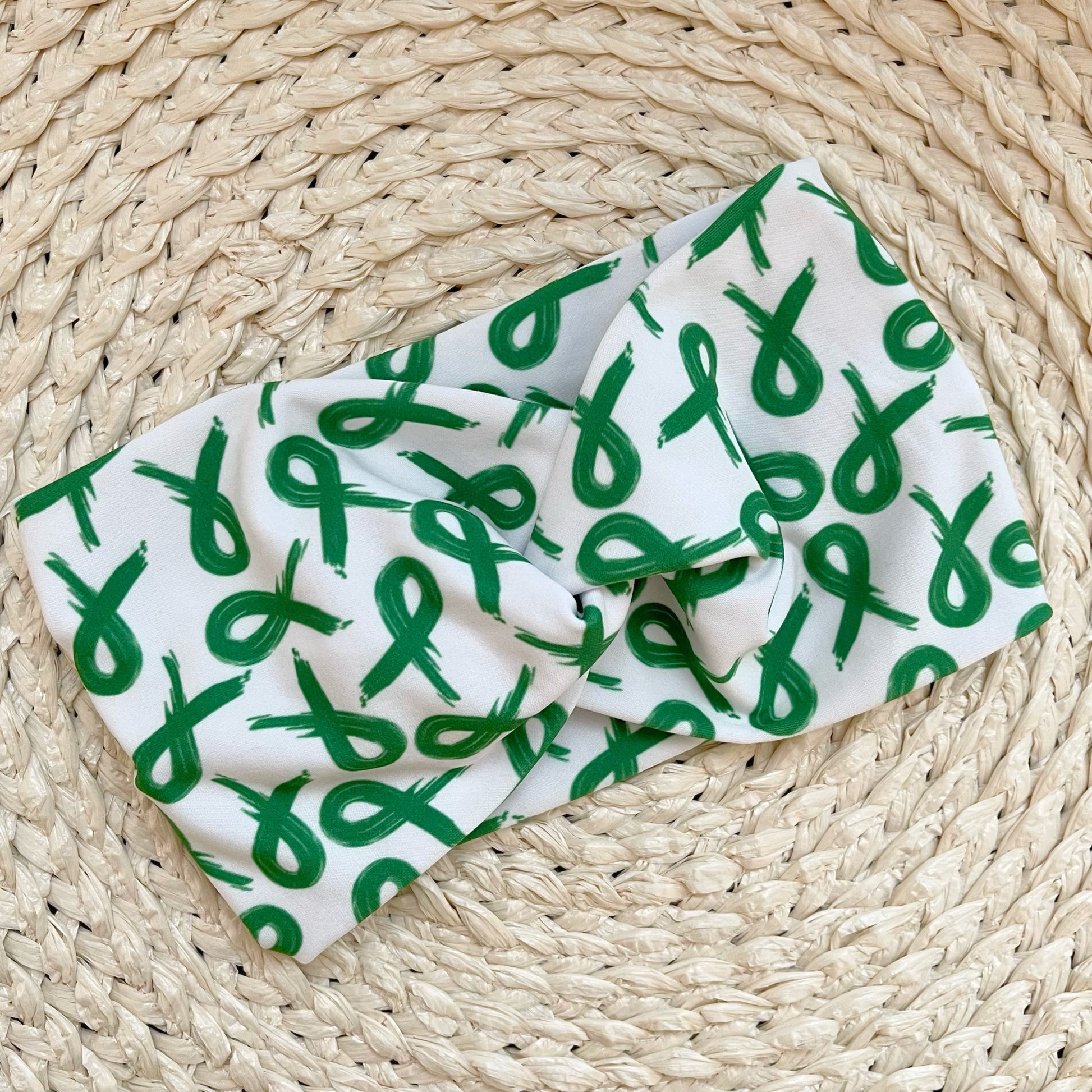 Wide, twisted, white headband with green ribbon print.