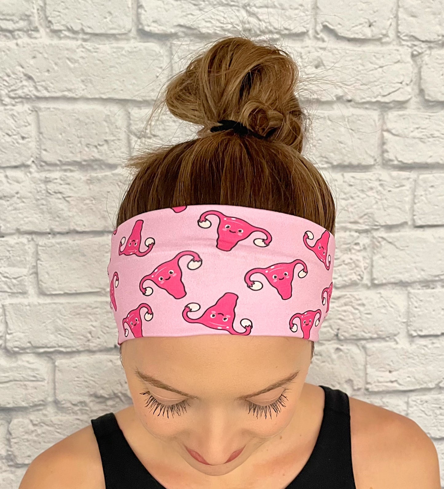 Woman with hair in bun wearing flat, stretchy, pink headband with uterus and ovaries print.