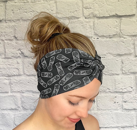 Woman with hair in bun wearing wide, twisted headband in black with white bandage print.