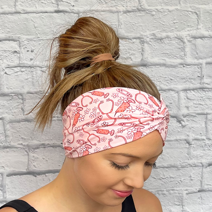 Woman wearing wide, twisted headband in pink with flowers, stethoscopes, bandages, and syringes.