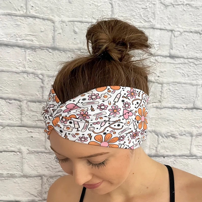 Woman wearing wide twisted, white headband with orange and pink medical theme print. Contains hearts, flowers, stethoscopes, bandages, and syringes.