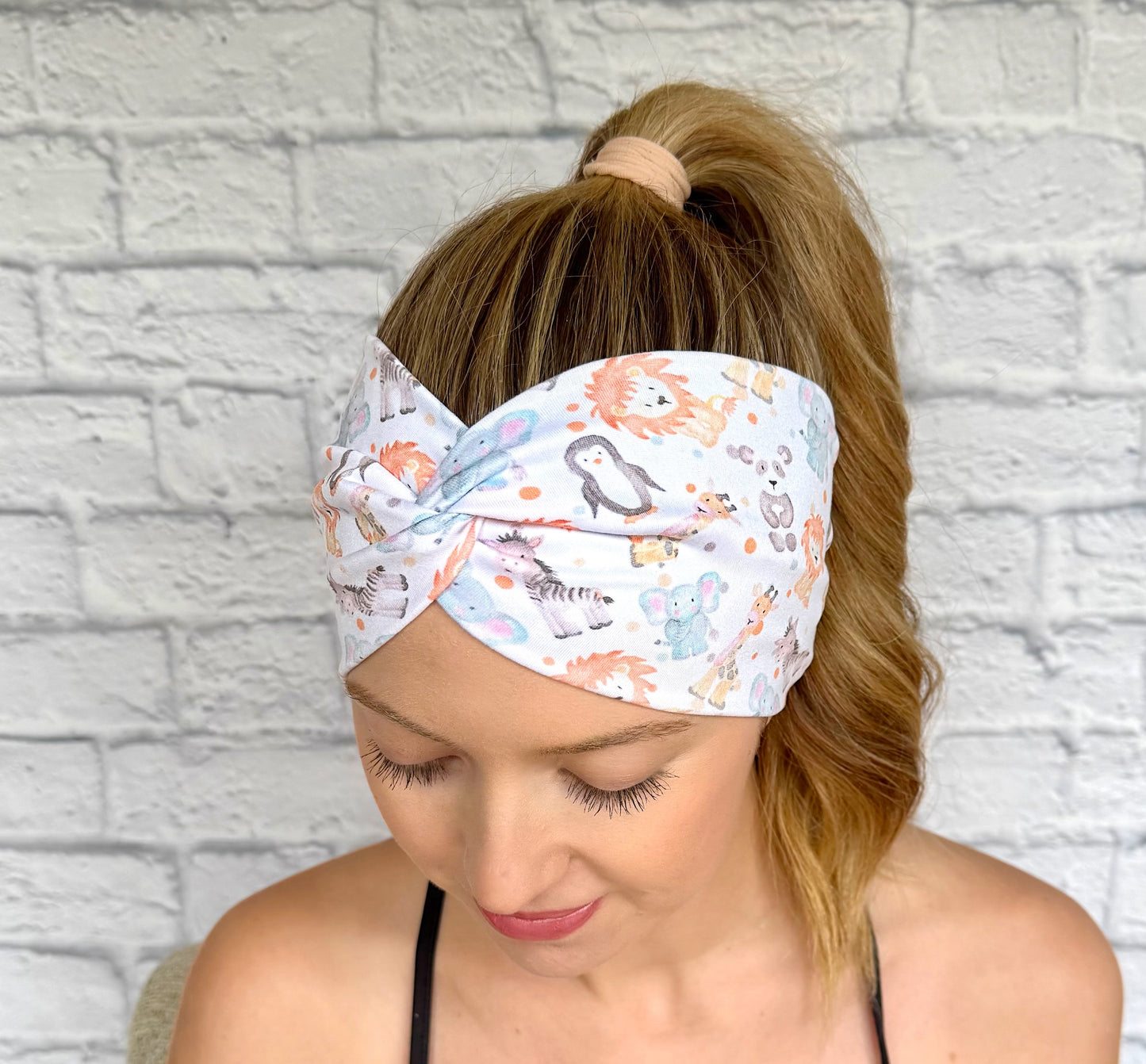 Woman with hair in ponytail wearing wide, twisted headband in white with baby animal and polka dot print.