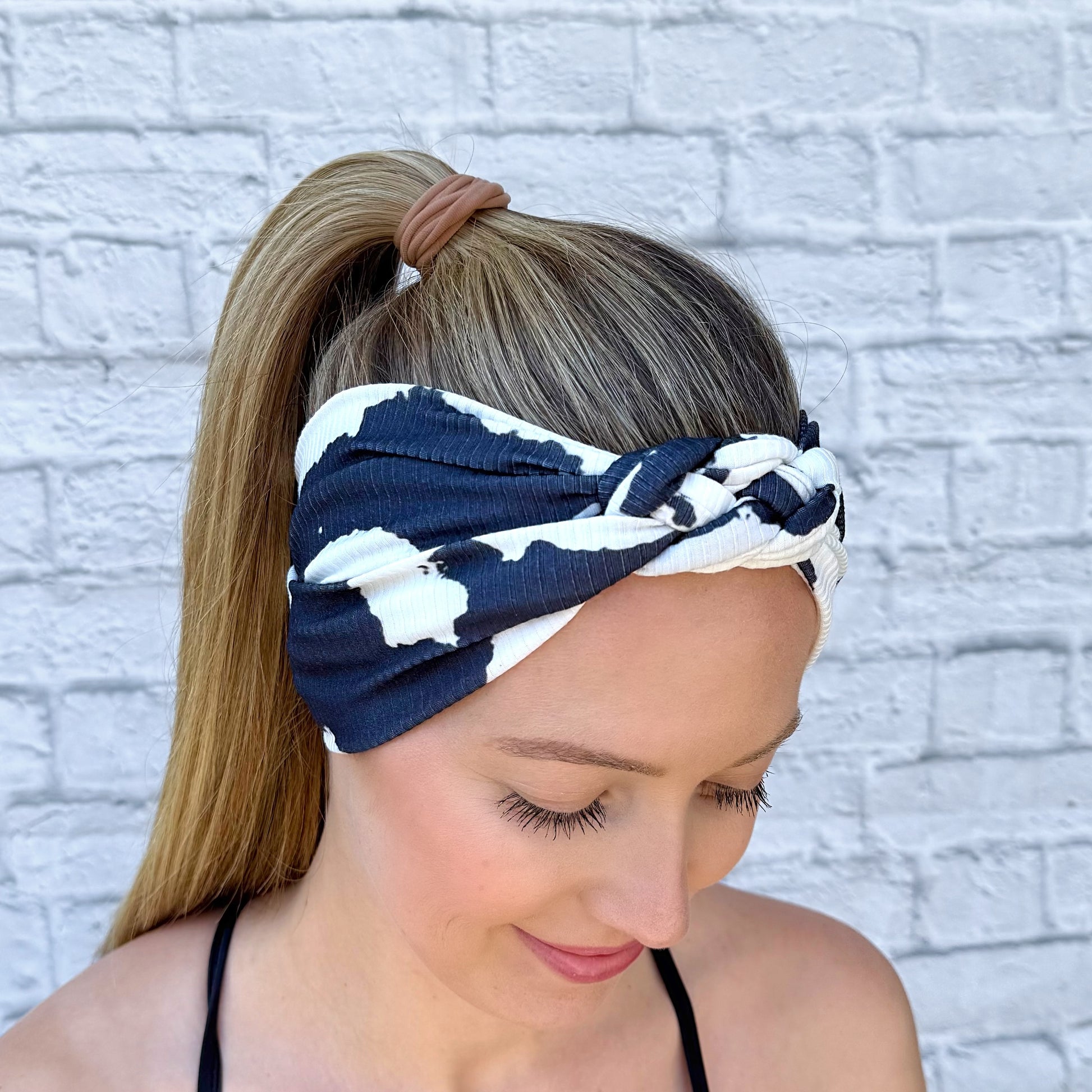 Woman with hair in ponytail wearing black and white cow print headband in sailor knot style with ribbed fabric.