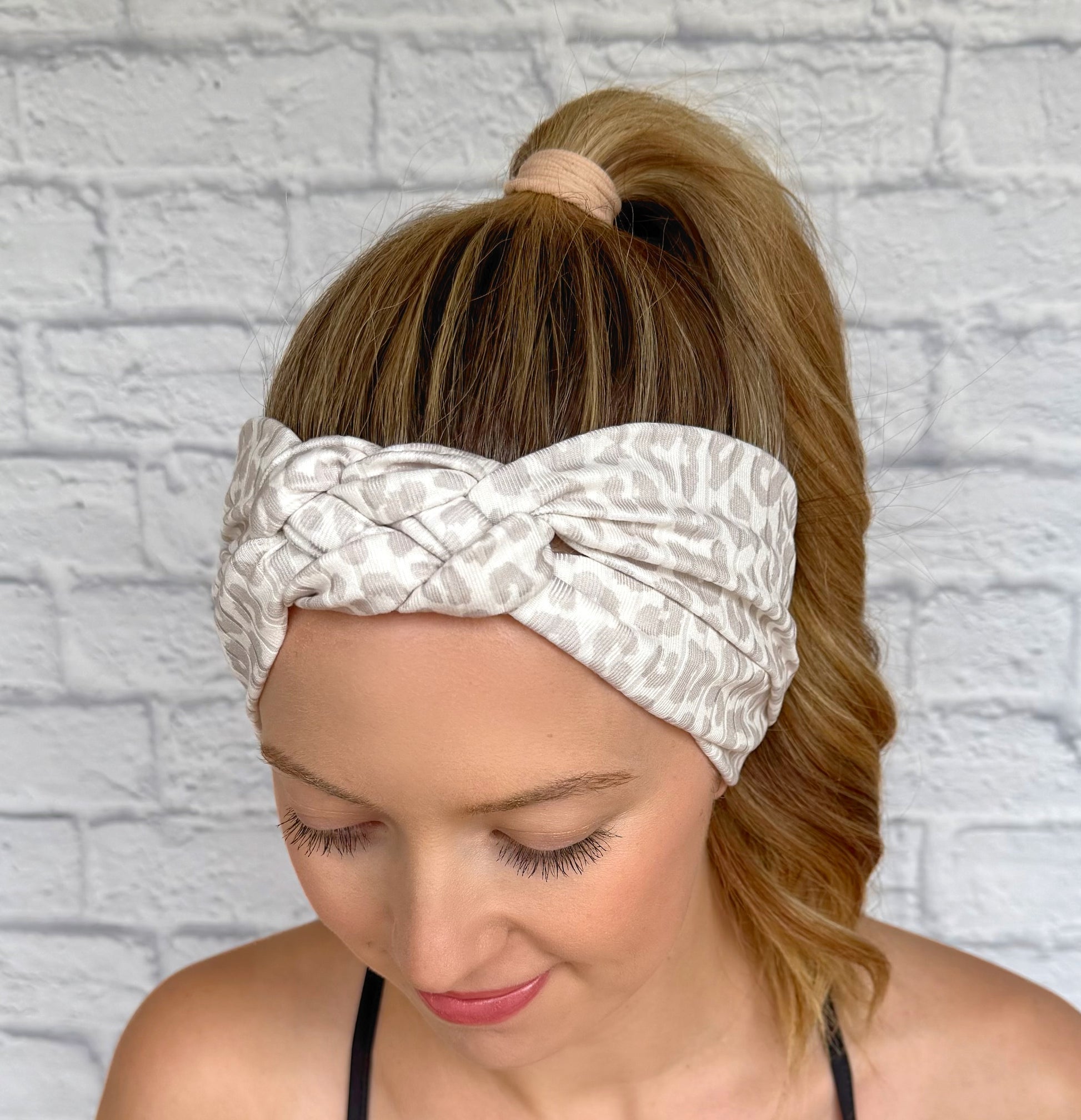 Woman with hair in ponytail wearing tan and white cheetah print headband in sailor knot style with ribbed fabric.