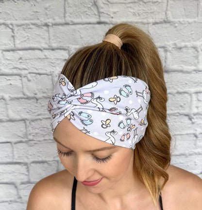Woman with hair in curled ponytail wearing wide, twisted, light gray headband with stork and baby theme print.