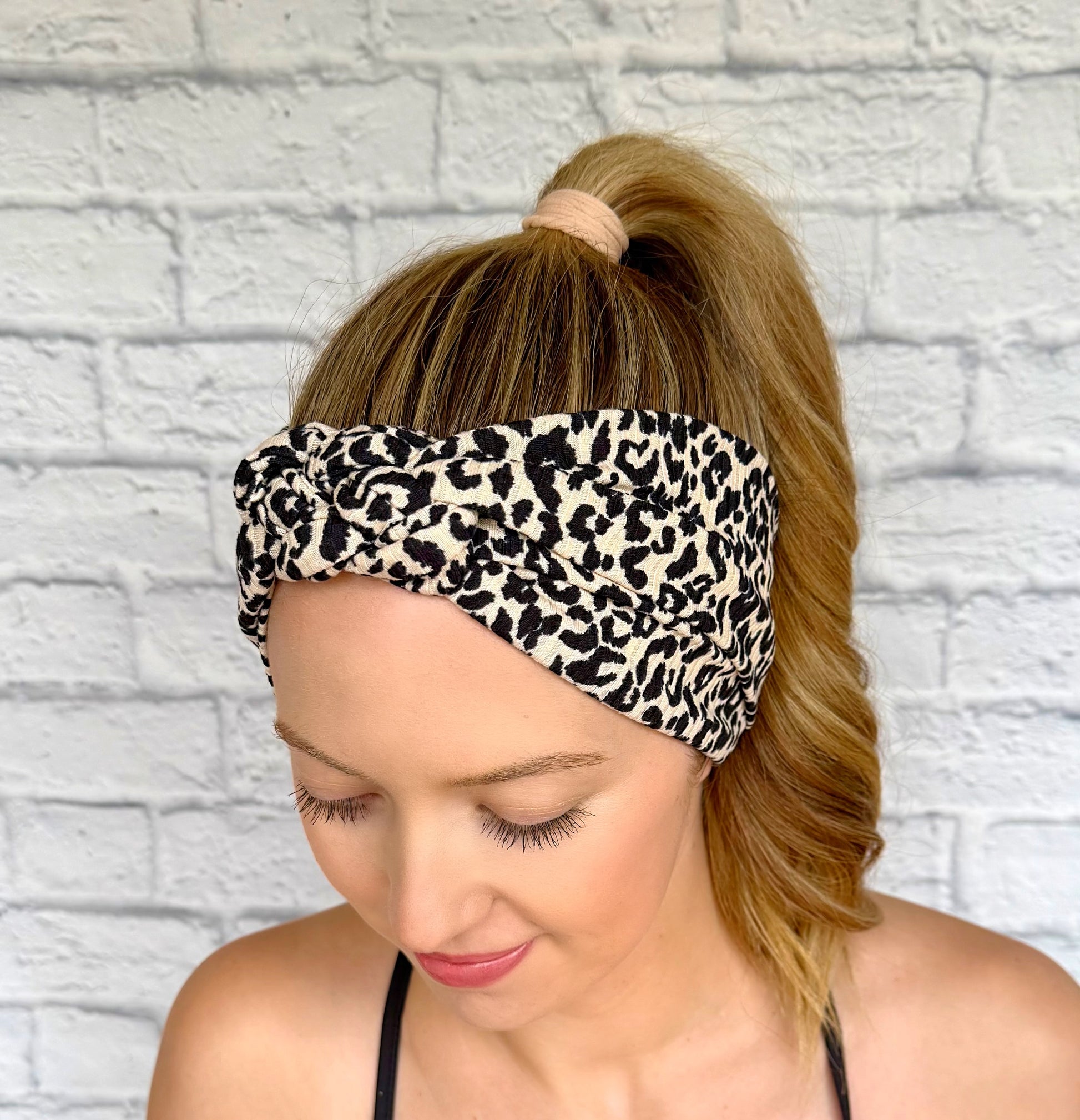 Woman with hair in curled ponytail wearing tan/cream color with black leopard print headband in sailor knot style.