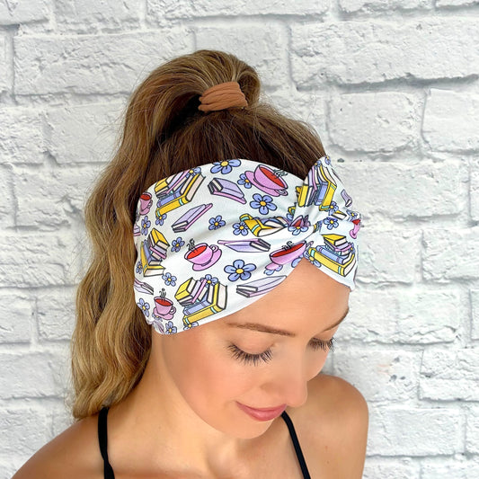 Woman with hair in ponytail wearing wide, twisted, white headband with coffee, flower, and book print.