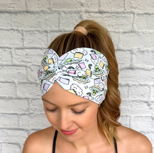 Woman with hair in ponytail wearing wide, twisted, light blue headband with alien theme print.