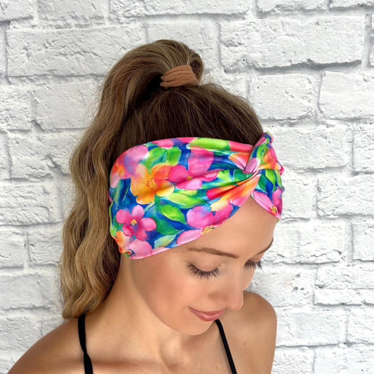 Woman with hair in ponytail wearing wide, twisted headband in blue with bright, multi-color Hawaiian theme floral print.
