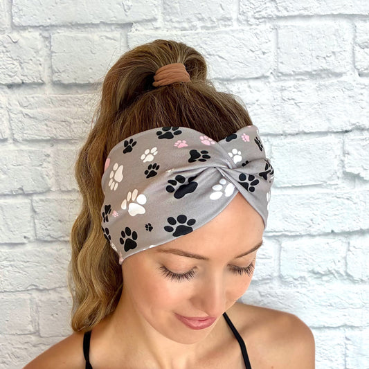 Woman with hair in ponytail wearing wide, twisted, gray headband with pink, black, and white dog paw print.