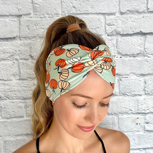 Woman with hair in ponytail wearing wide, twisted, stretchy, mint green headband with pumpkin print.