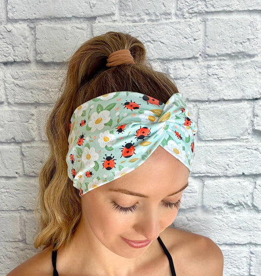 Woman wearing a headband with ladybug and flower pattern against a white brick wall.
