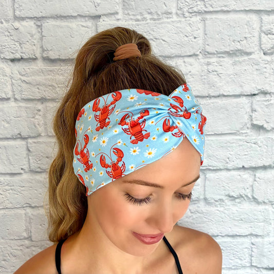 Woman with hair in ponytail wearing wide, twisted, light blue headband with lobster and white floral print.