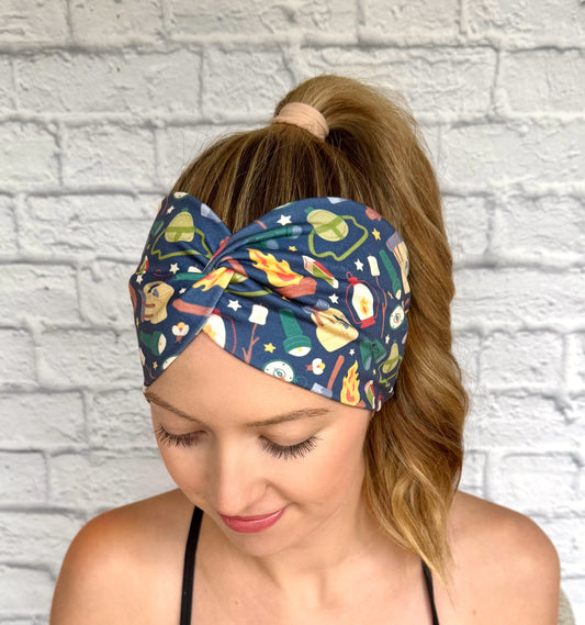 Woman with hair in curly ponytail wearing wide, twisted, navy blue headband with camping theme print.