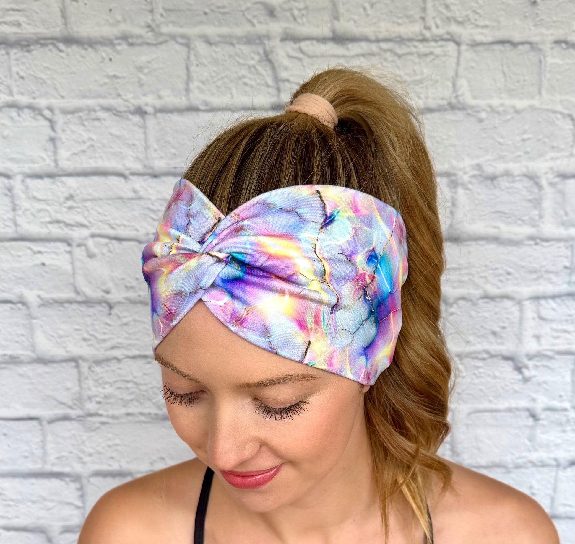 Woman with hair in ponytail wearing wide, twisted headband with multi-color watercolor print.