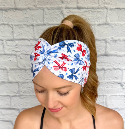 Woman with hair in ponytail wearing wide, twisted, white headband with red and blue bows and blue star print.