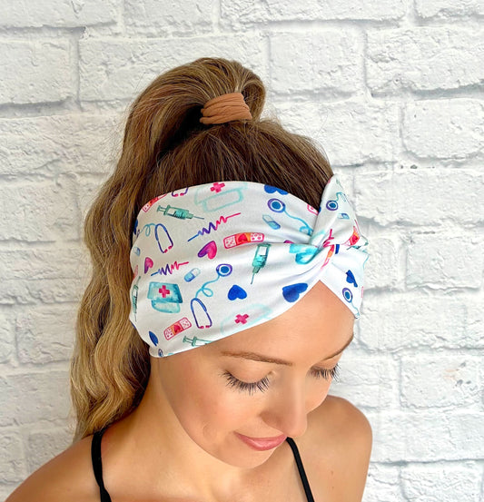 Woman with hair in ponytail wearing wide, twisted, white headband with pink, blue, and purple medical theme print.
