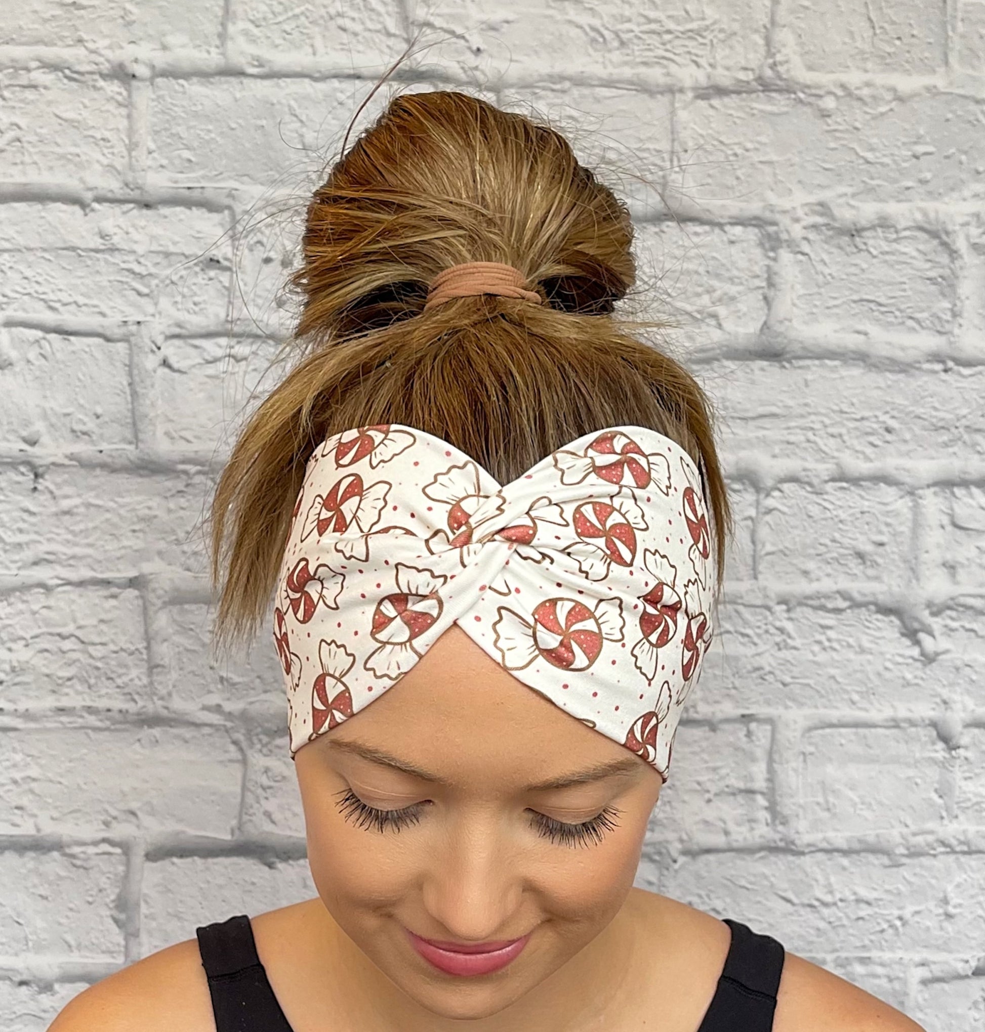 Woman with hair in bun wearing wide, twisted, white headband with red peppermint print.