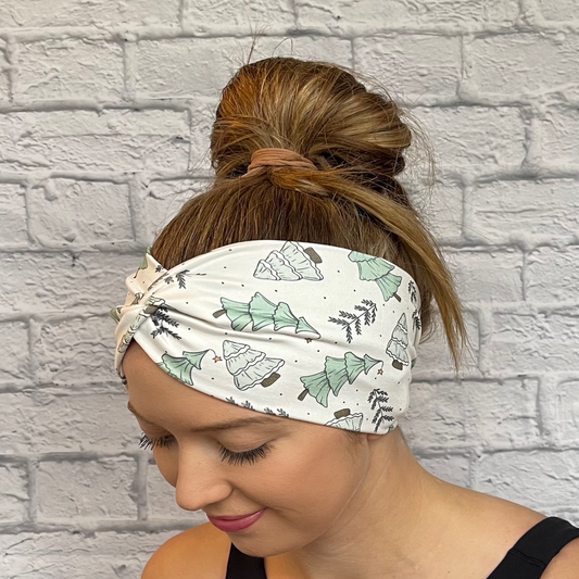 Woman with hair in bun wearing white, wide, twisted headband with light green Christmas trees.