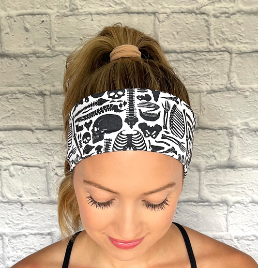 Woman with hair in curled ponytail wearing flat, stretchy headband in white with black skeleton print.