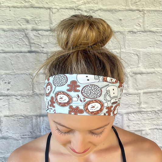 Woman with hair in bun wearing stretchy, light blue headband with snowman, gingerbread, and hot chocolate print.