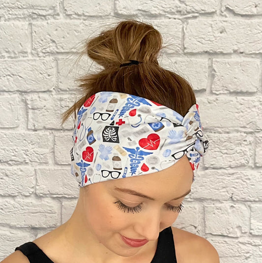 Woman with hair in bun wearing wide, twisted headband in light blue, red, and black medical theme print.