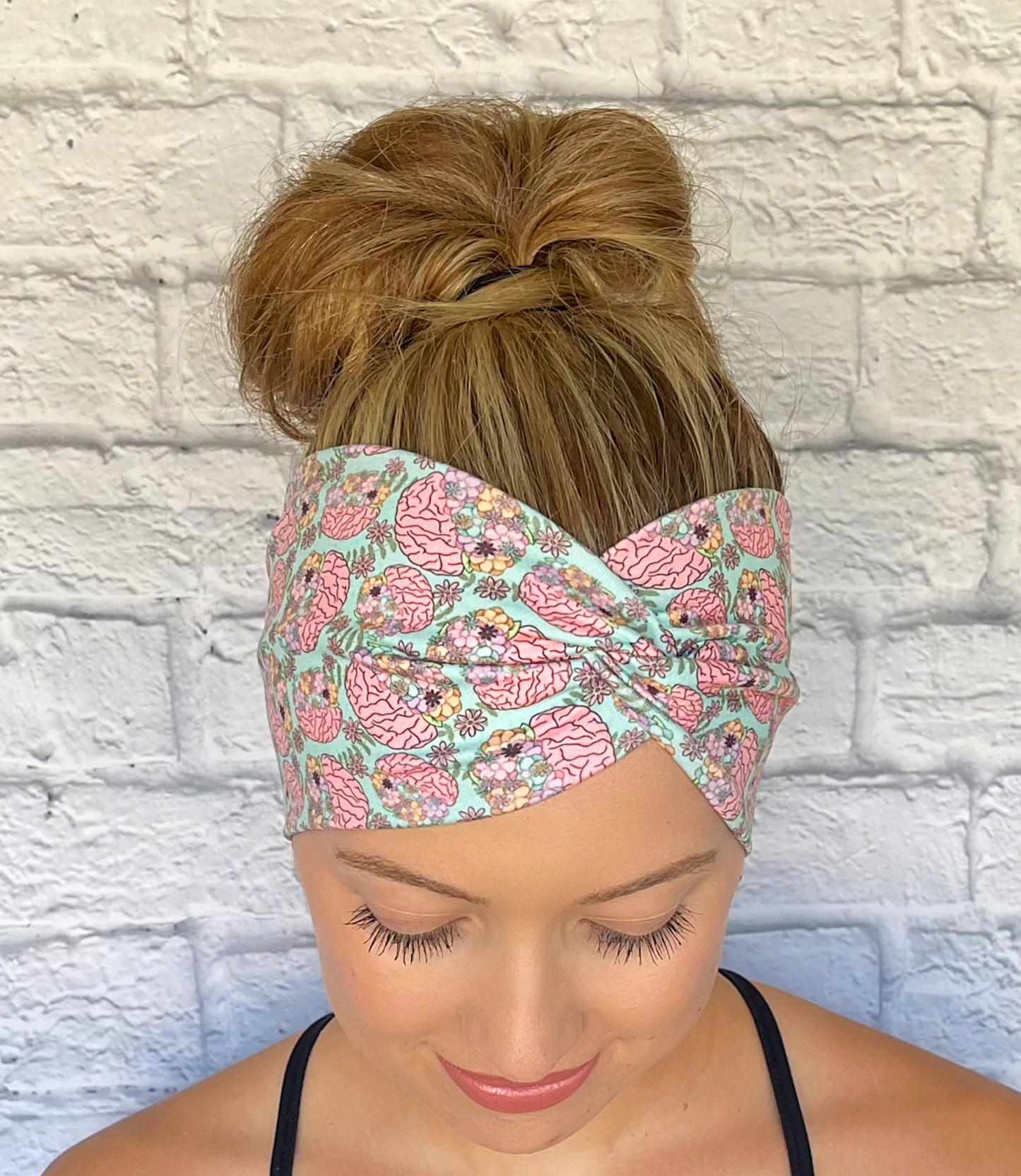 Woman with hair in bun wearing wide, twisted headband in mint green color with brain and flower print.