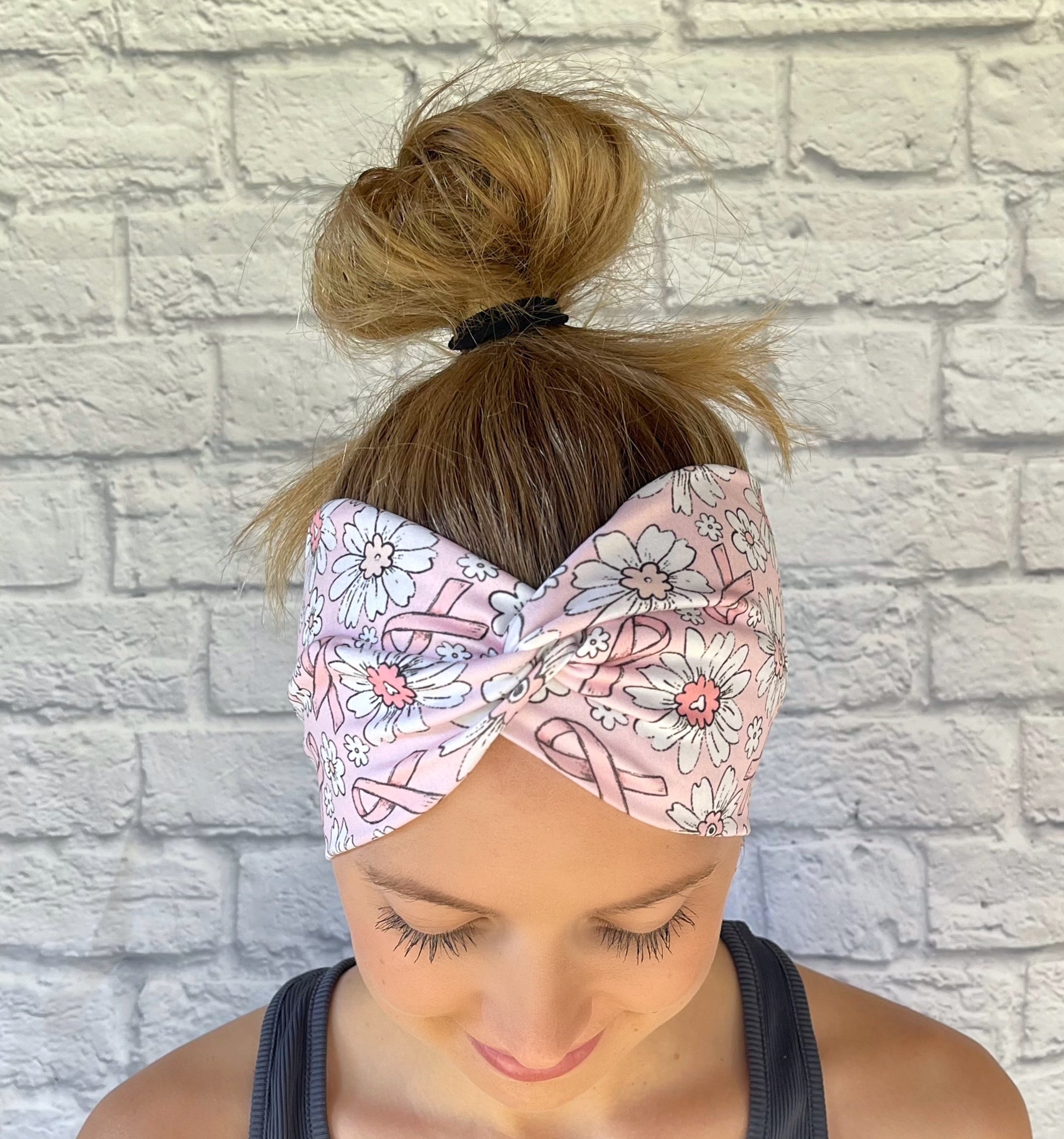 Woman with hair in bun wearing light pink, wide, twisted headband with pink ribbon and white flower print.