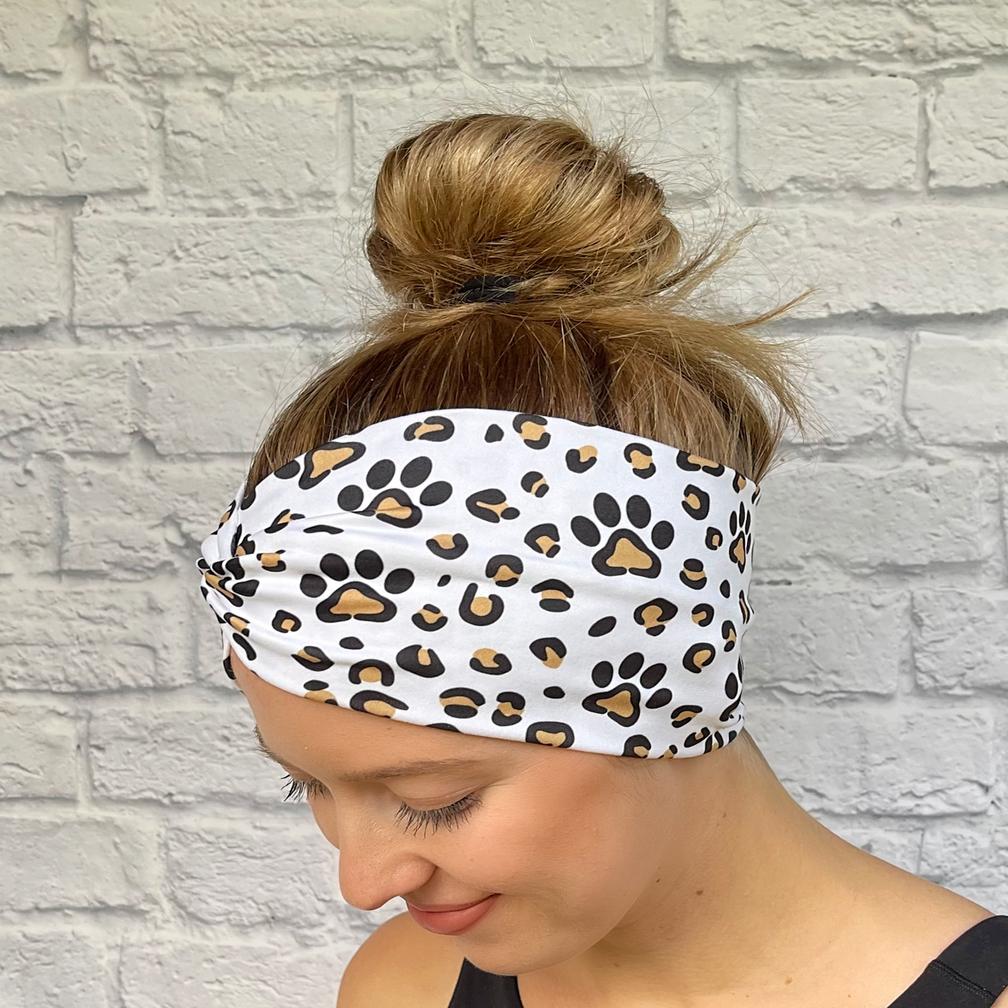 Woman with hair in bun wearing wide, white, twisted headband with brown and black dog paws and cheetah print. 