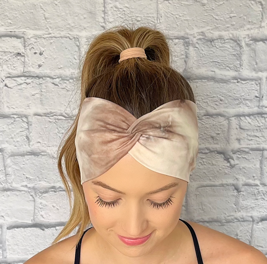 Woman with hair in curled ponytail wearing wide, twisted headband in light brown tie dye print.