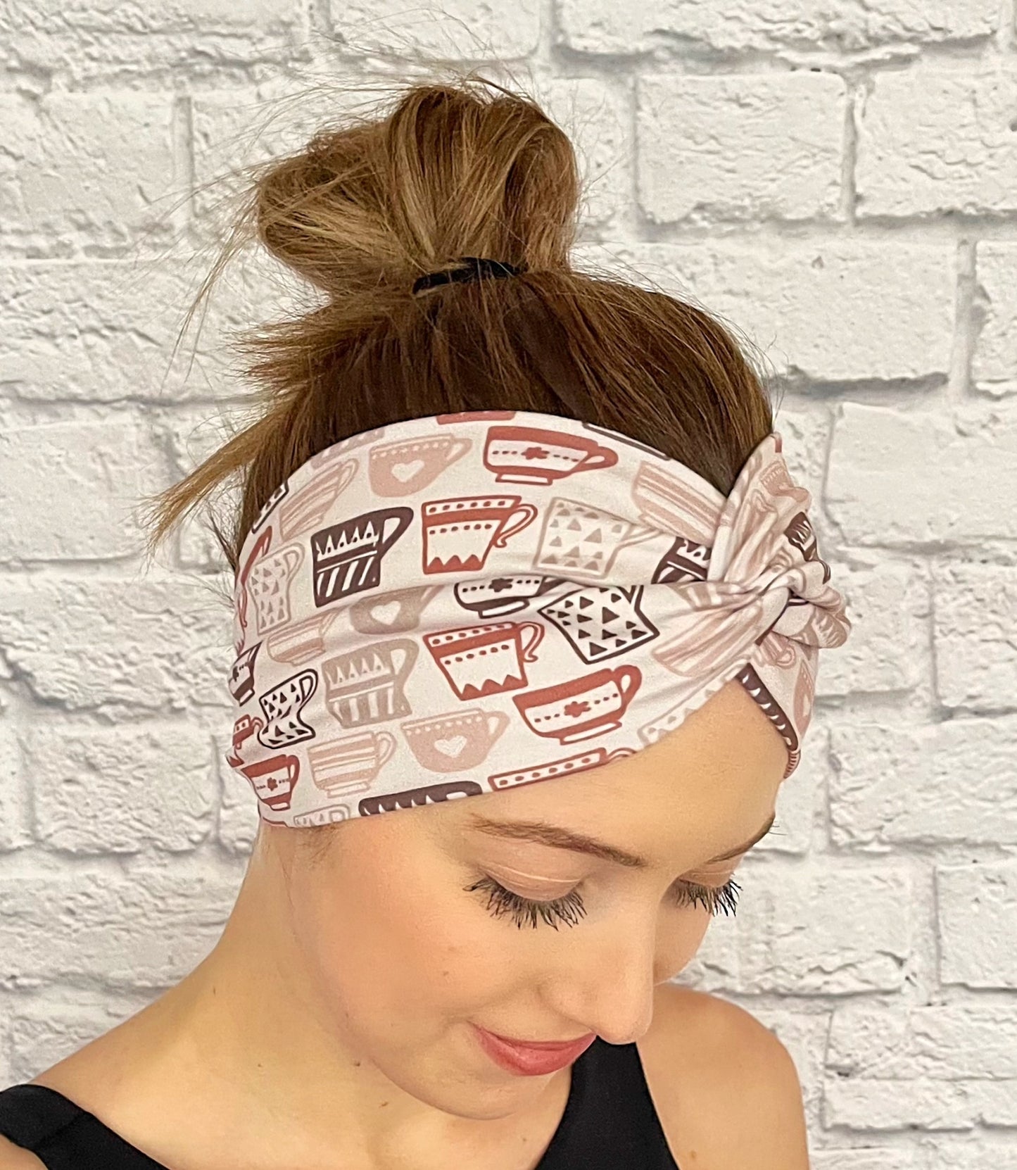 Woman with hair in bun wearing wide, twisted headband in light brown with brown coffee cup print.