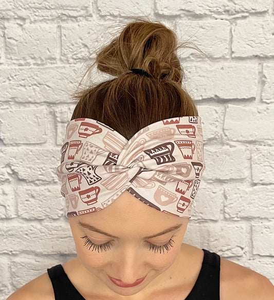 Woman with hair in bun wearing wide, twisted headband in light brown with brown coffee cup print.