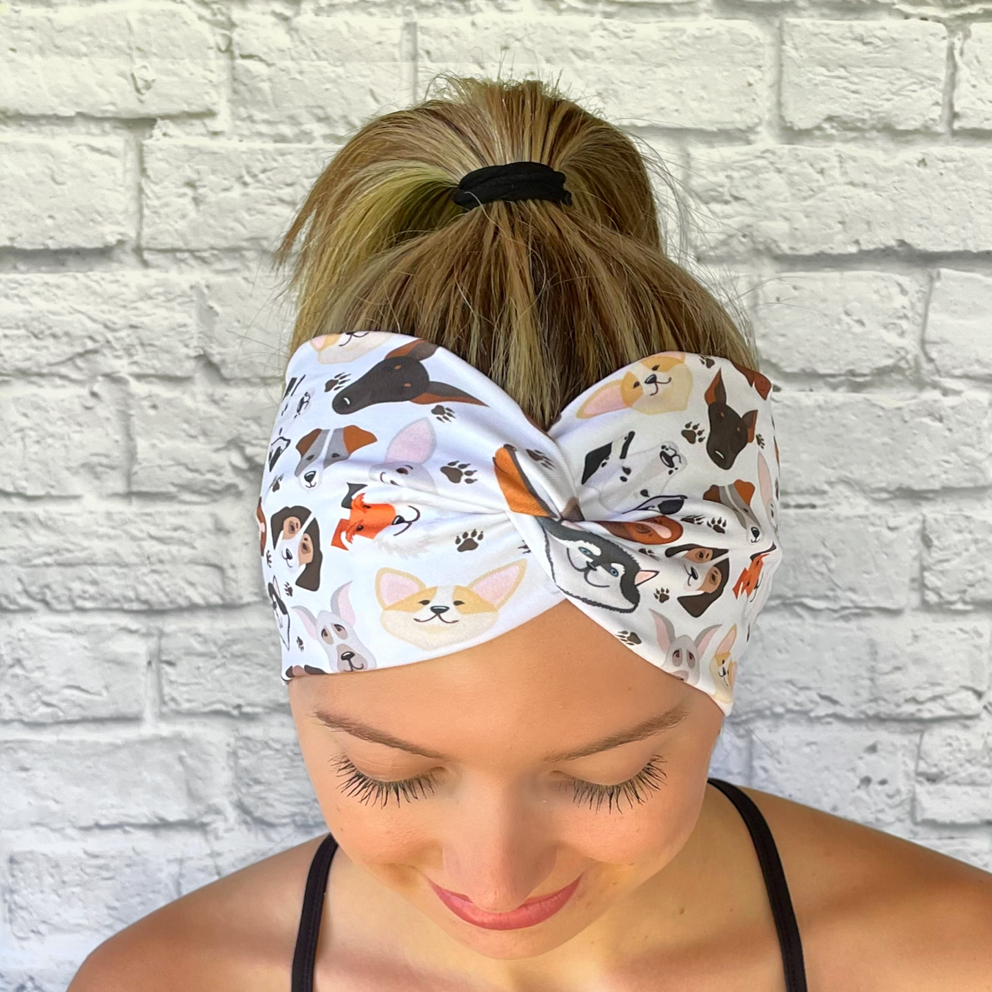 Woman with hair in ponytail wearing white, wide twisted headband with dog theme print.