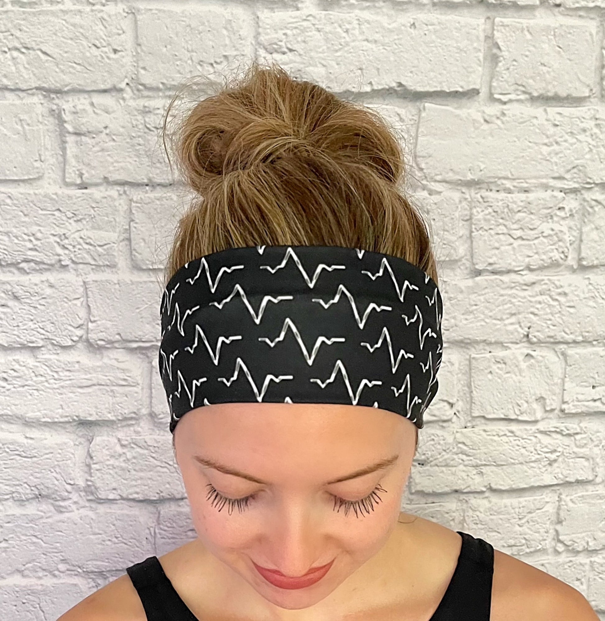 Woman with hair in bun wearing black, stretchy headband with white EKG print.