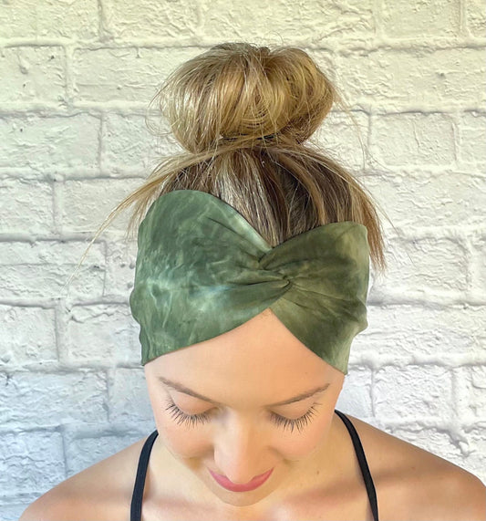 Woman with hair in bun wearing wide, twisted headband in green tie dye print.