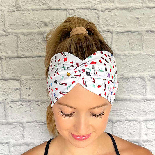 Woman with hair in ponytail wearing white, wide twist headband with phlebotomy theme print.