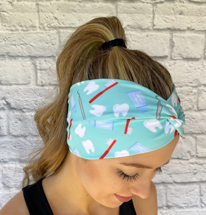 Woman with hair in curled ponytail wearing stretchy, wide, twisted headband in mint color with dental theme print.