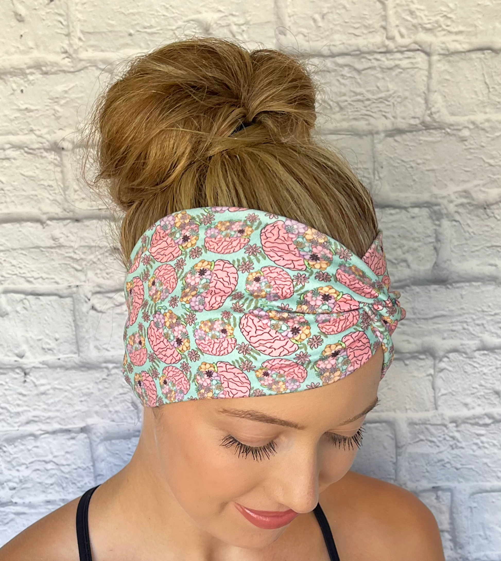 Woman with hair in bun wearing wide, twisted headband in mint green color with brain and flower print.