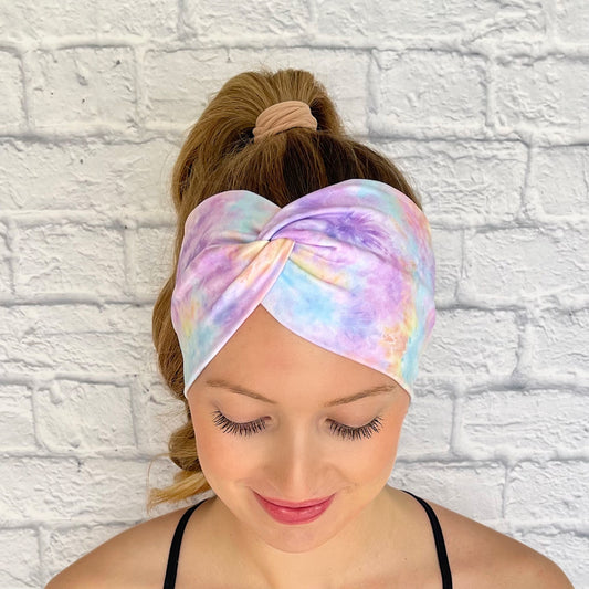 Woman with hair in curled ponytail wearing wide, twisted headband with pastel color tie dye print.