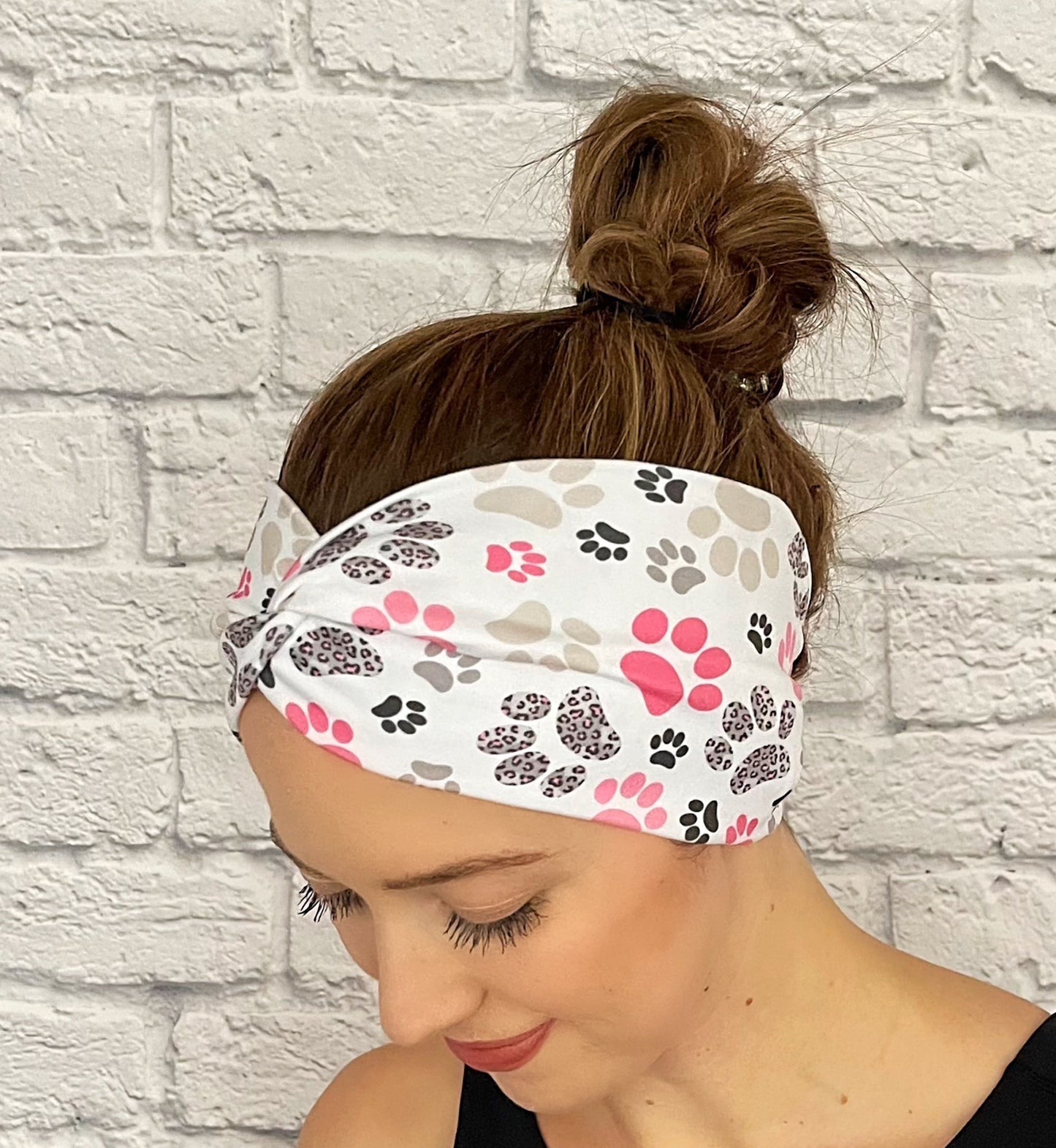 Woman with hair in bun wearing wide, twisted headband in white with pink, gray, and black paw print.