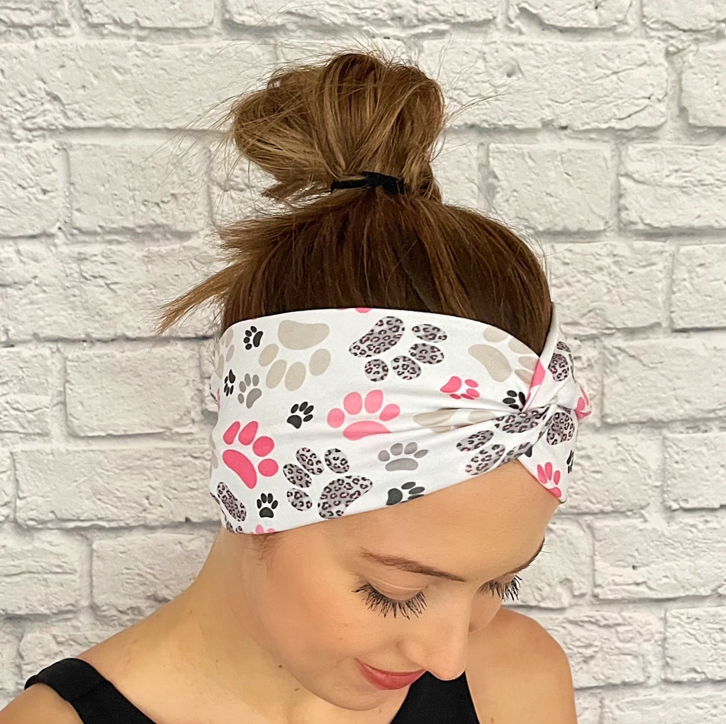 Woman with hair in bun wearing wide, twisted headband in white with pink, gray, and black paw print.