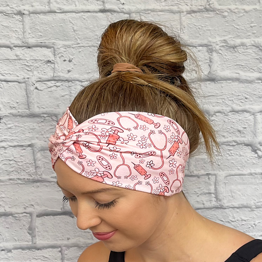 Woman wearing wide, twisted headband in pink with flowers, stethoscopes, bandages, and syringes.