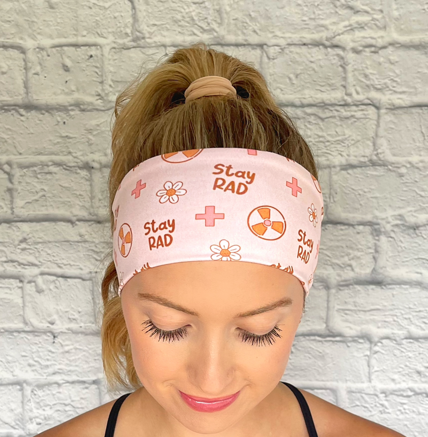 Woman with hair in curled ponytail wearing pink headband with "stay rad" print, radiology theme print, and flowers.
